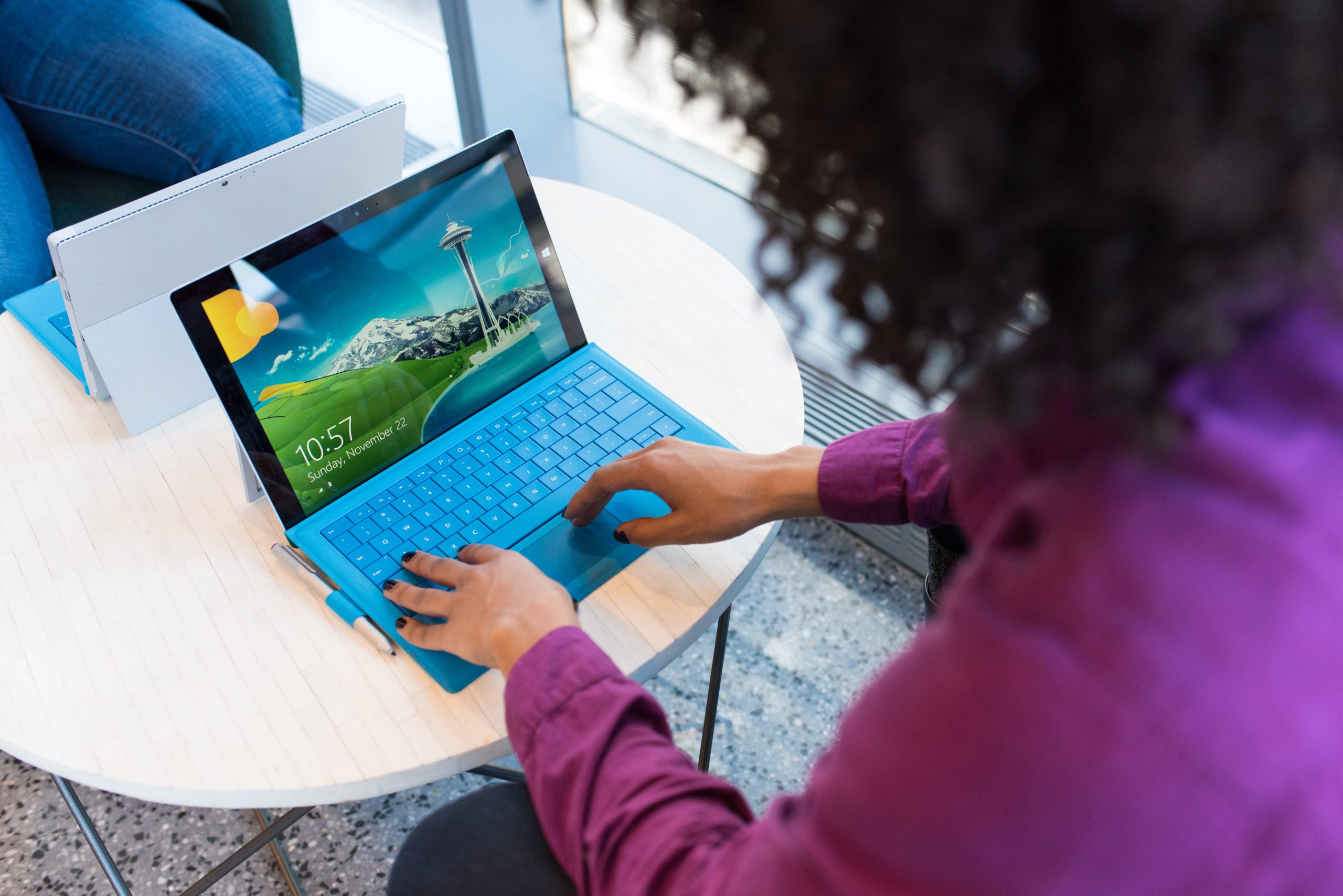 A person typing on a blue keyboard which is sat underneath a Windows Surface computer