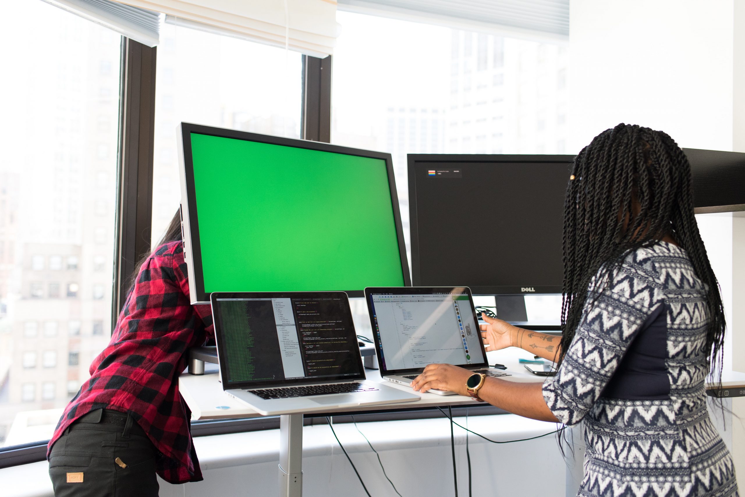 Two people at a desk with one behind two large screens and two laptop computers