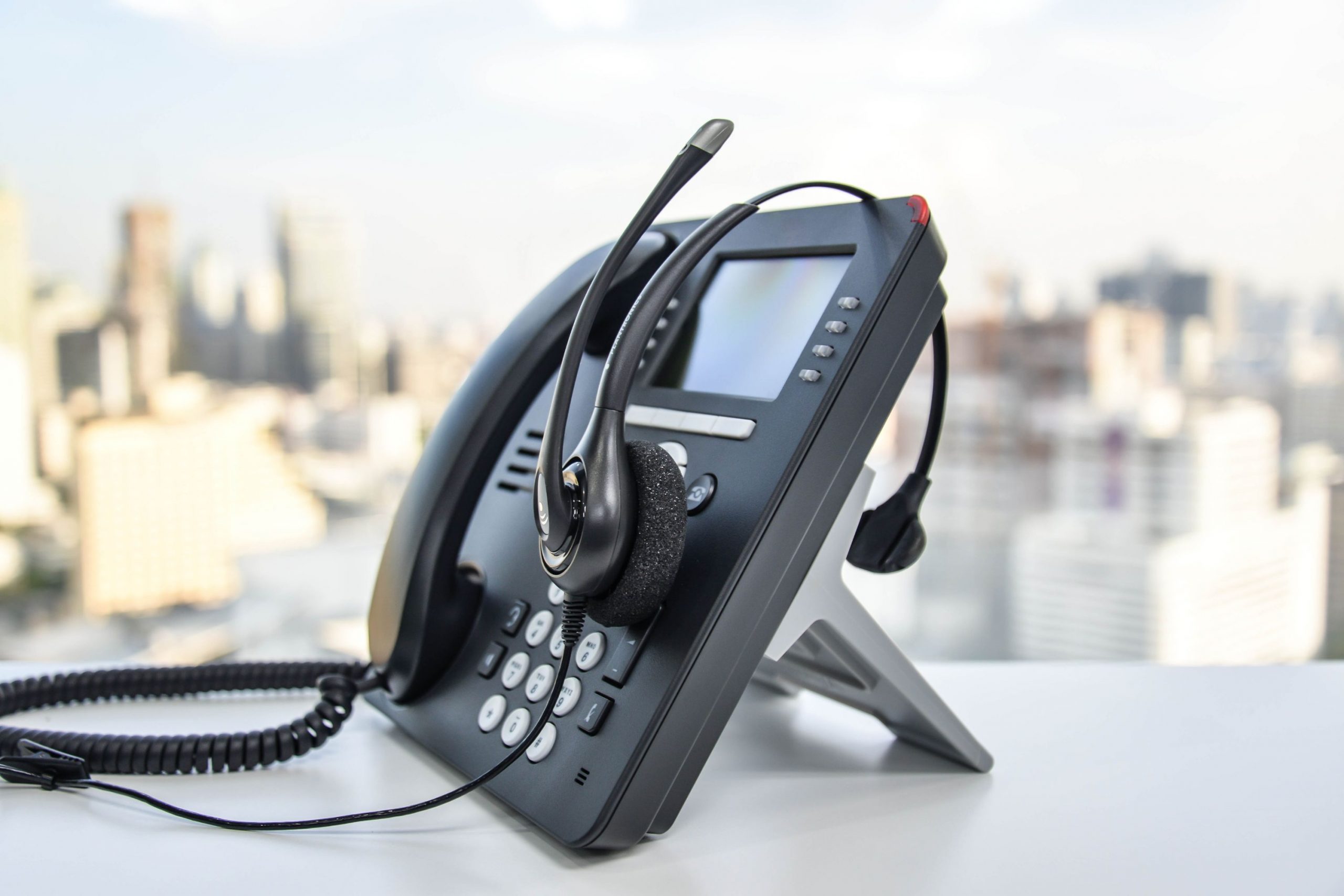 A desk phone sat on a white table with a headset placed on top of the phone