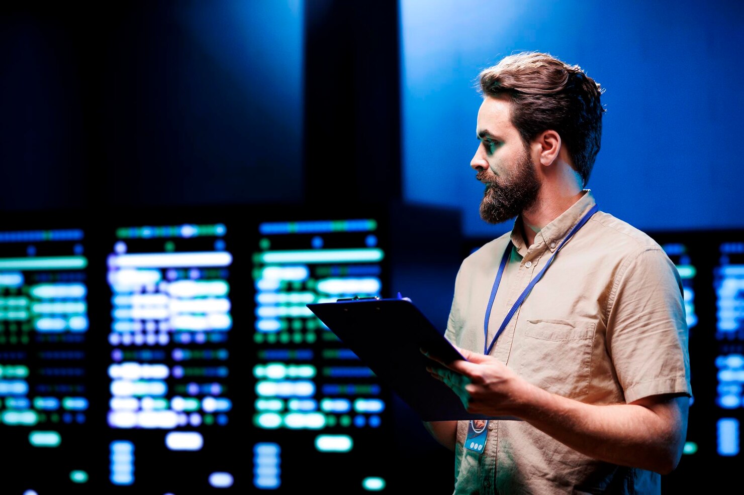 A man with pale coloured shirt stood with a clipboard in a security operations centre