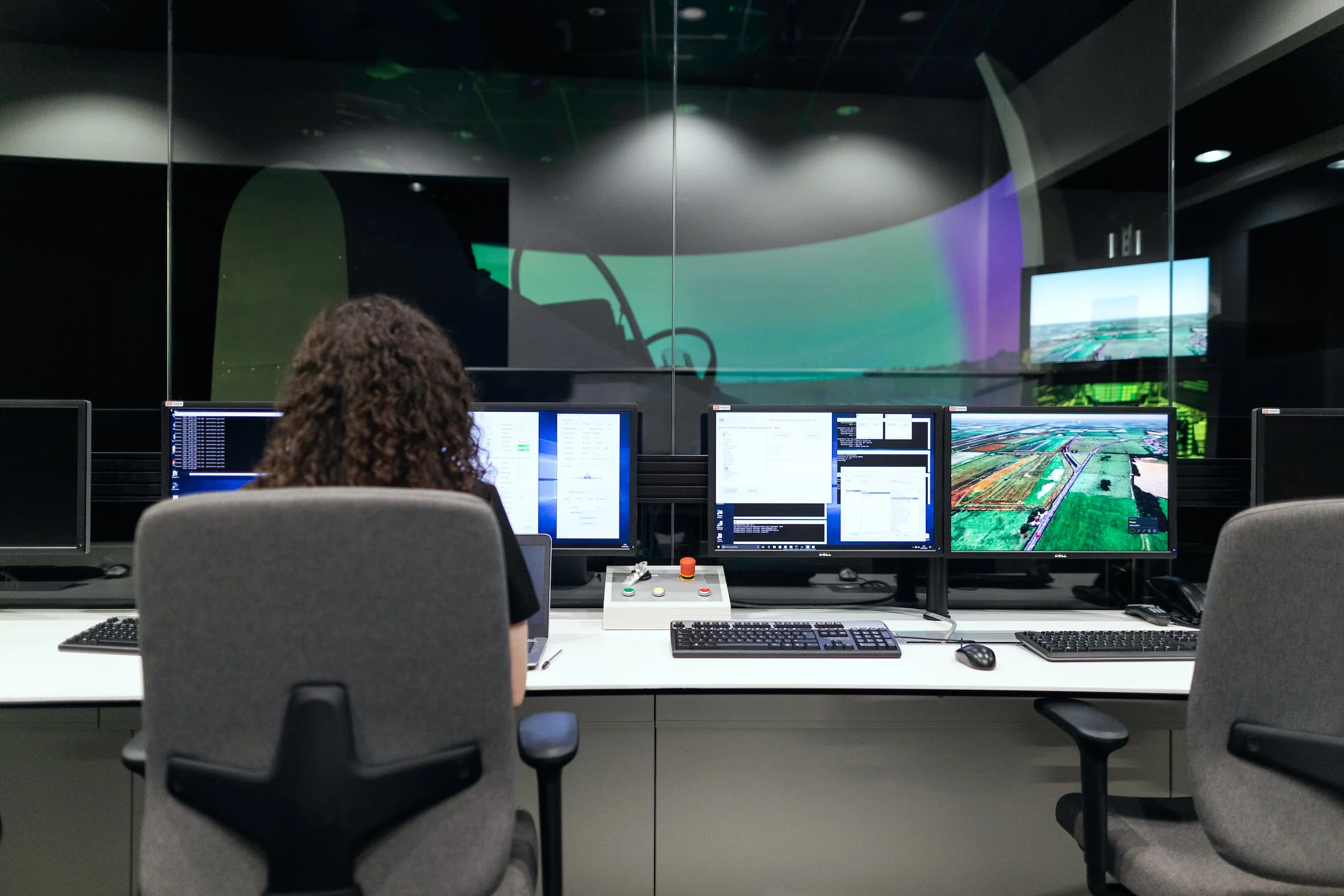 A person with black hair sat at a desk of four computers