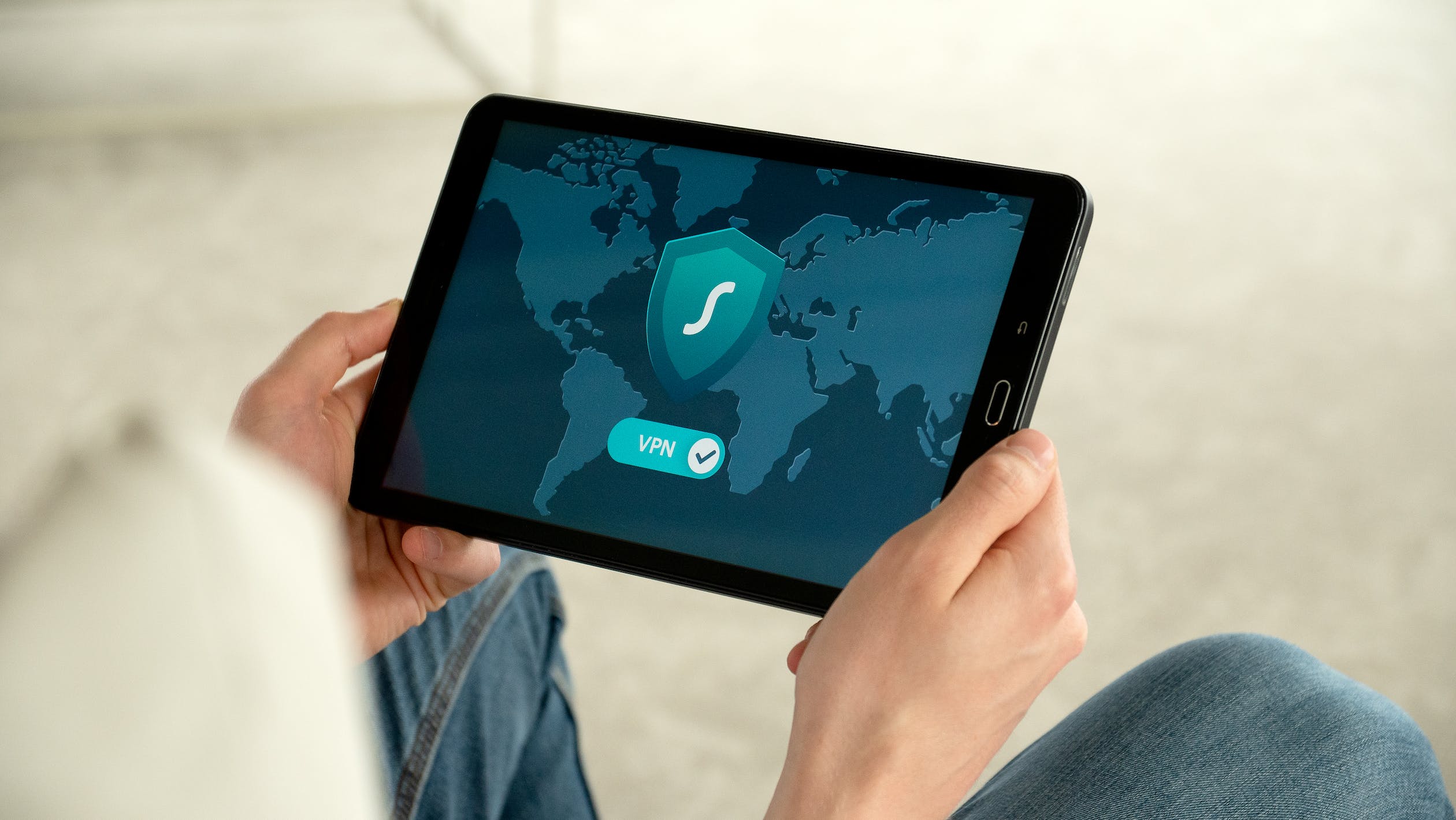 A person viewing a Samsung tablet screen displaying VPN with a map of the world behind it