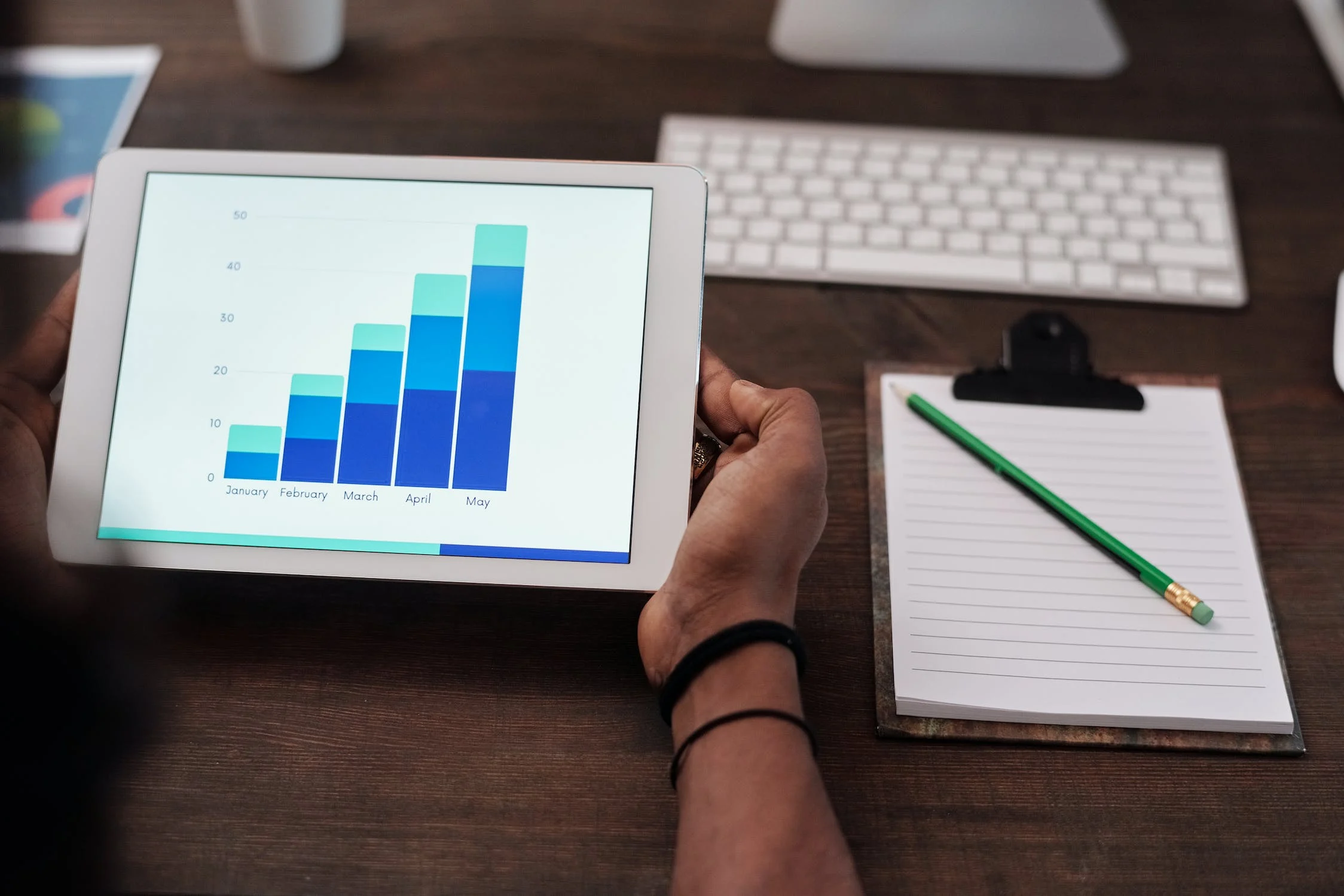 A person viewing monthly reporting charts at a desk with a notepad with pencil sat next to them